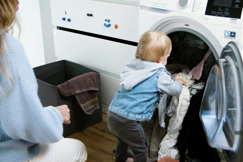 Adorable child assisting in laundry chores indoors with mother.